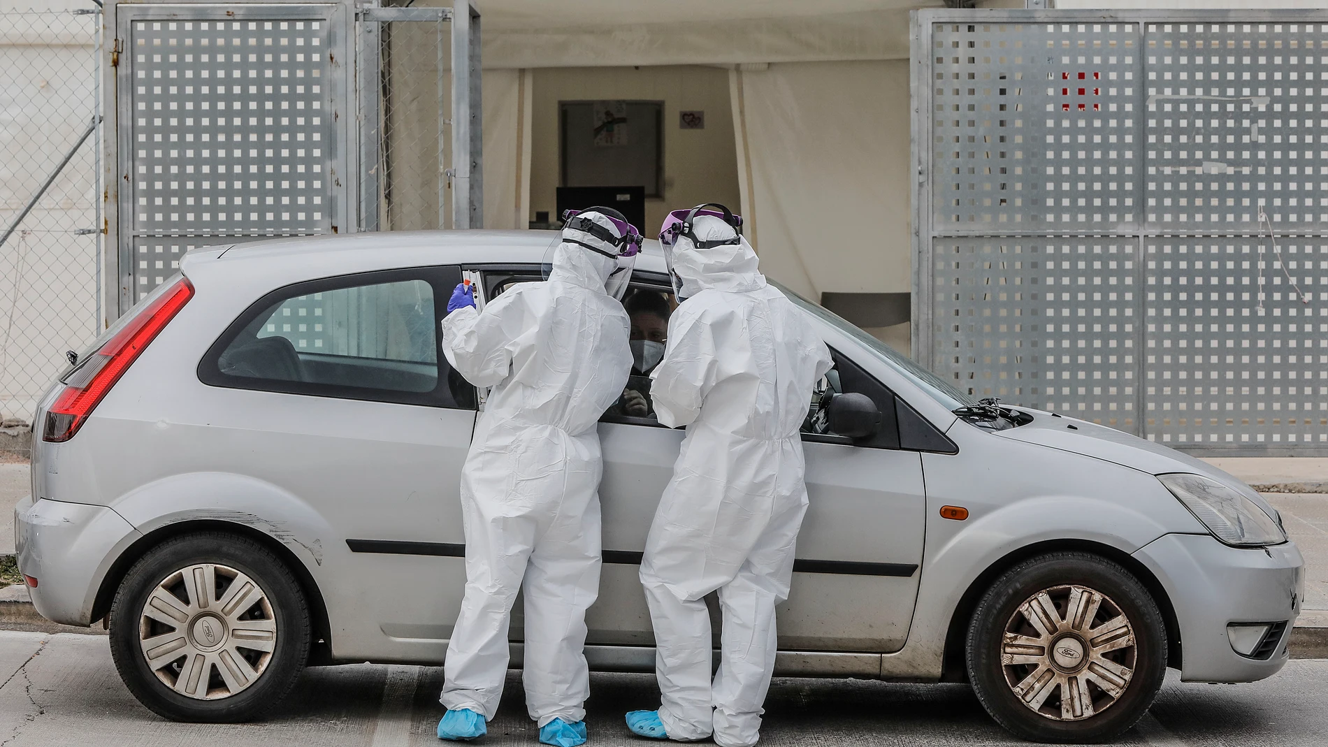 Dos sanitarios realizan una prueba PCR a una persona desde su vehículo