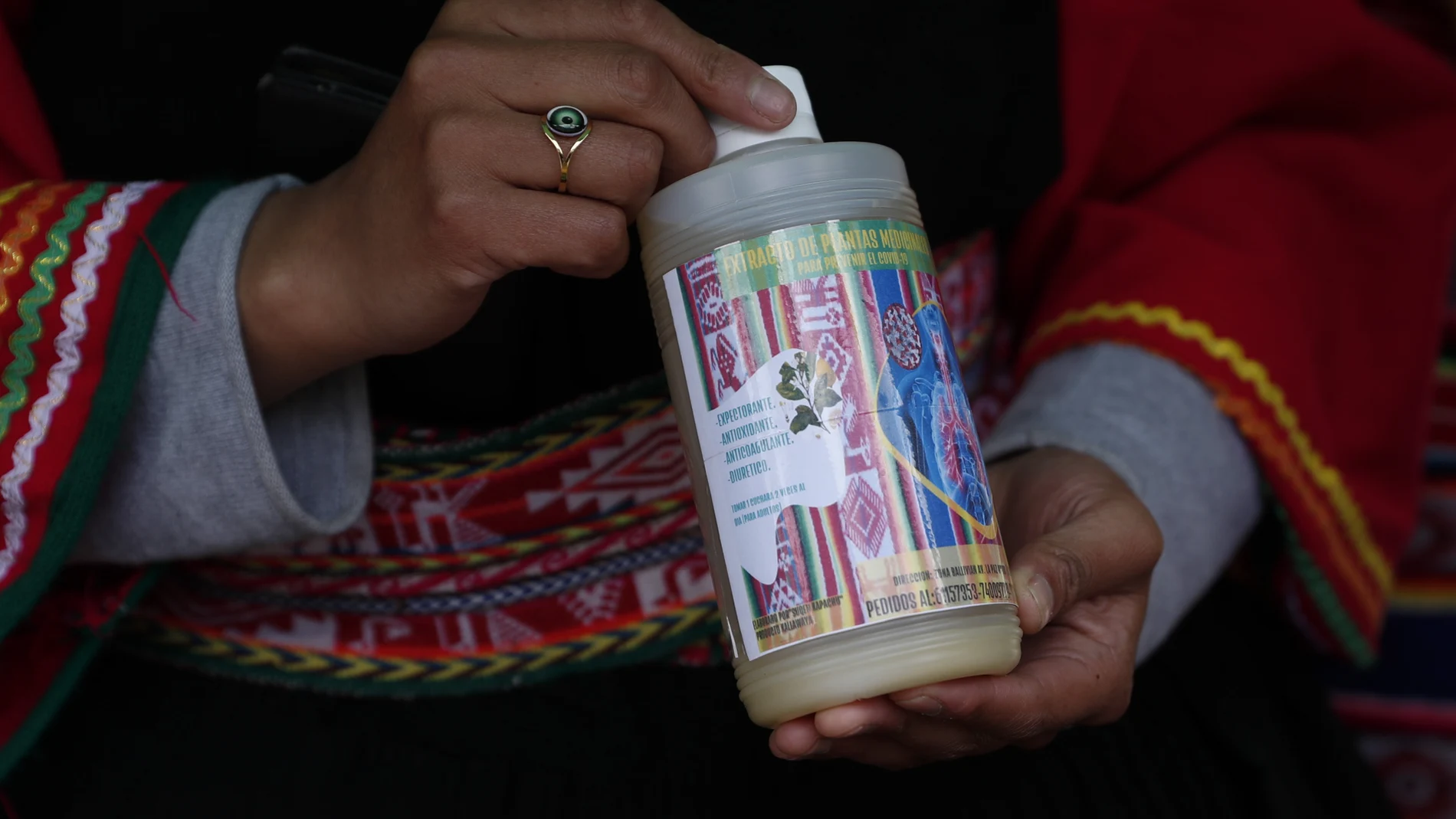 A traditional doctor holds a bottle of a medicinal herb extract, with a label that reads in Spanish "For the prevention of COVID-19," for sale at one of four exhibition booths set up by the government to promote the use of medicinal herbs in Plaza Bolivia in La Paz, Bolivia, Tuesday, Jan. 26, 2021. (AP Photo/Juan Karita)