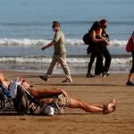 Dos personas toman el sol en la Playa de la Malvarrosa (Comunidad Valenciana) mientras otras pasean por la orilla