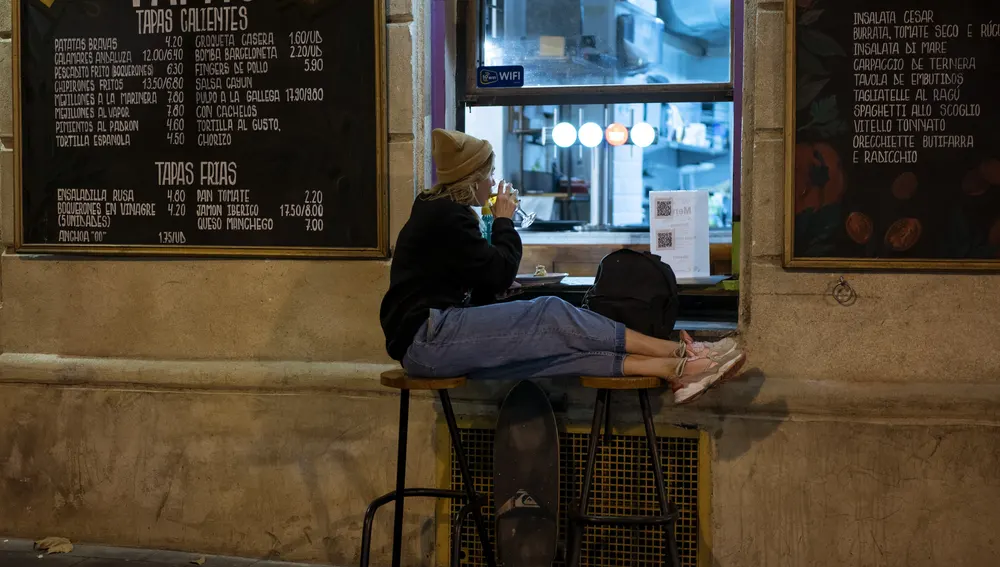 Una joven bebe una copa de vino sola en el exterior de un bar de Barcelona