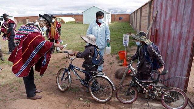 An Aymaran Indigenous parent gives anti-bacterial gel to students entering the Jancohaqui Tana school, where students are wearing new, protective uniforms as they return for their first week of in-person classes amid the COVID-19 pandemic, near Jesus de Machaca, Bolivia, Thursday, Feb. 4, 2021. (AP Photo/Juan Karita)