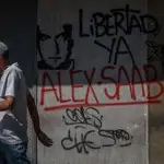 Un hombre camina junto a una pared con un graffiti que pide la libertad de Álex Saab en Caracas