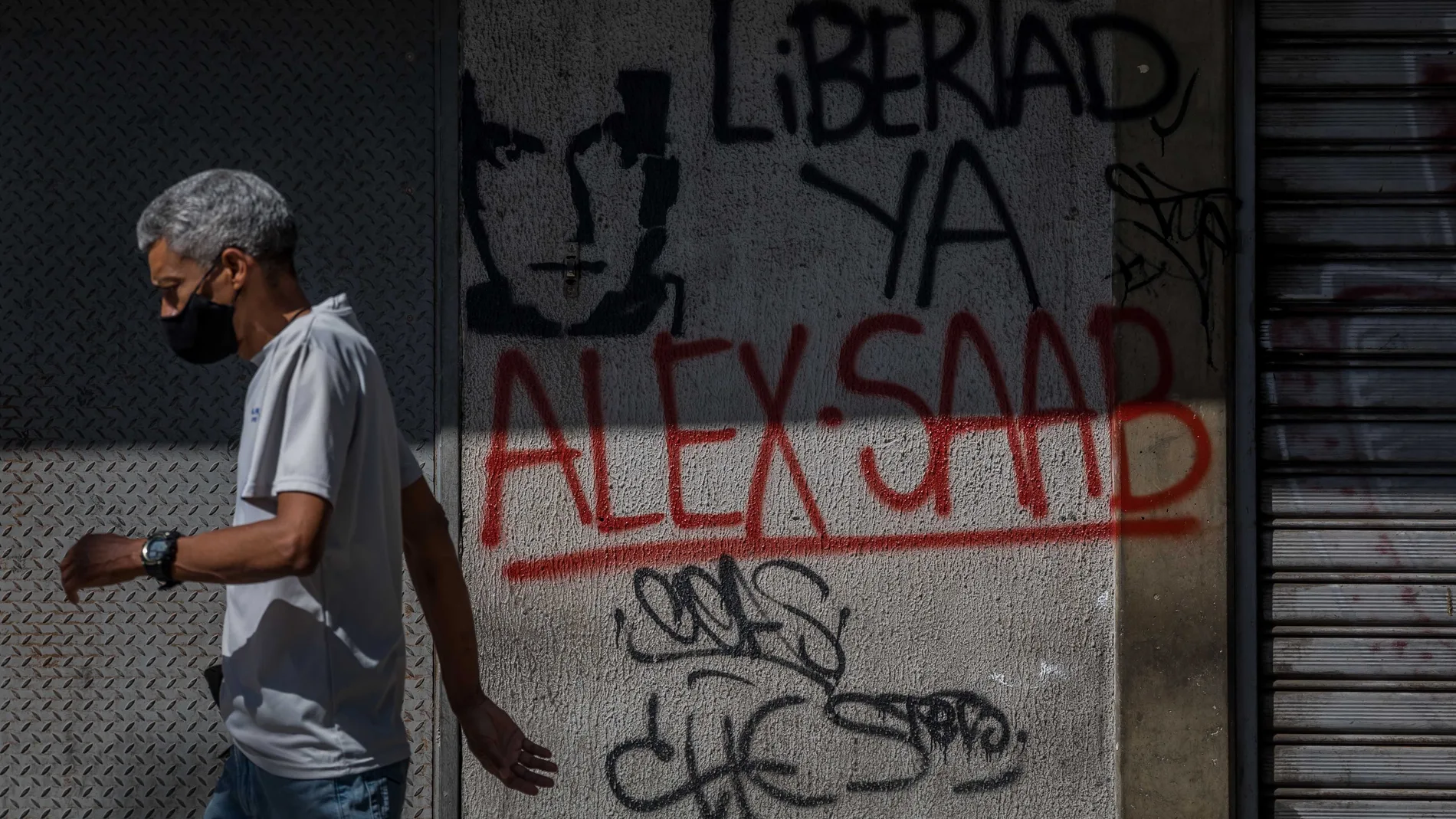 Un hombre camina junto a una pared con un graffiti que pide la libertad de Álex Saab en Caracas