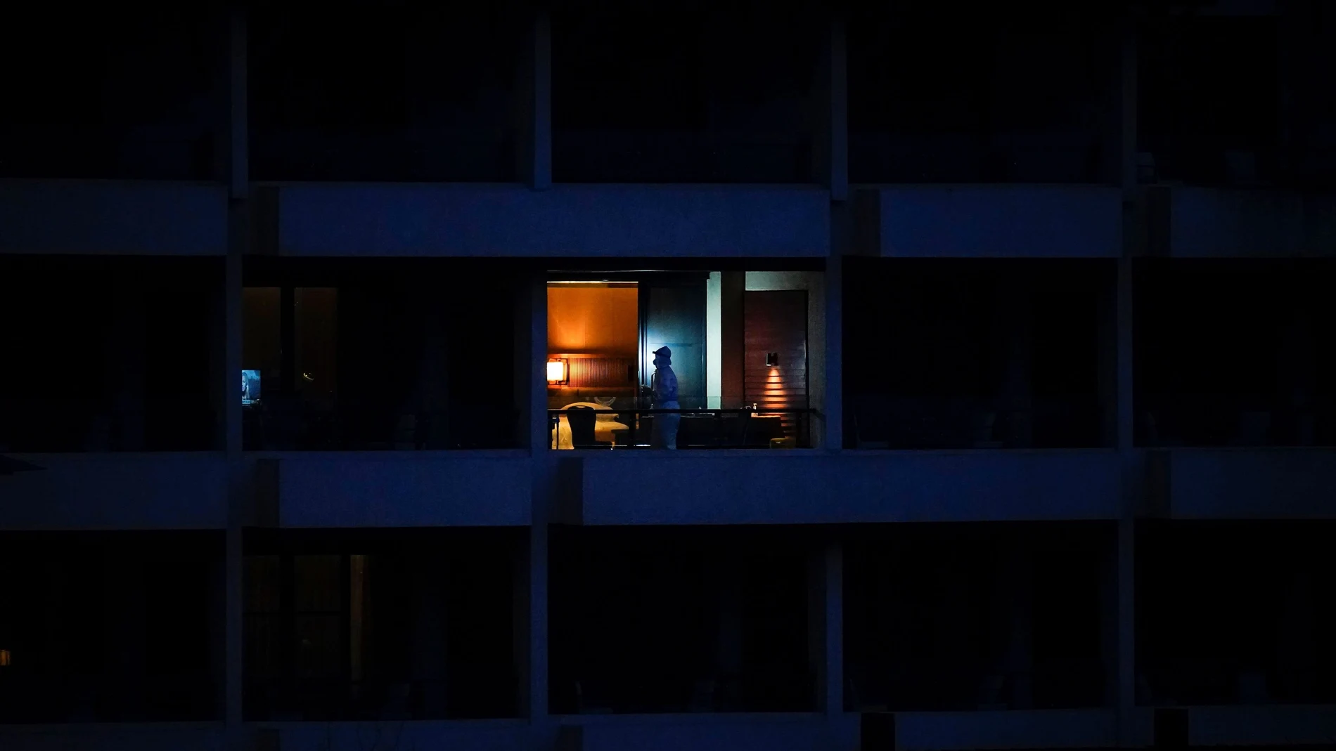 Una persona vestida con traje de protección se asoma al balcón del hotel donde fueron alojados los miembros de la delegación internacional de científicos
