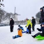 Unos niños se deslizan en trineo cerca de un molino de viento mientras nieva en Nijmegen, Países Bajos