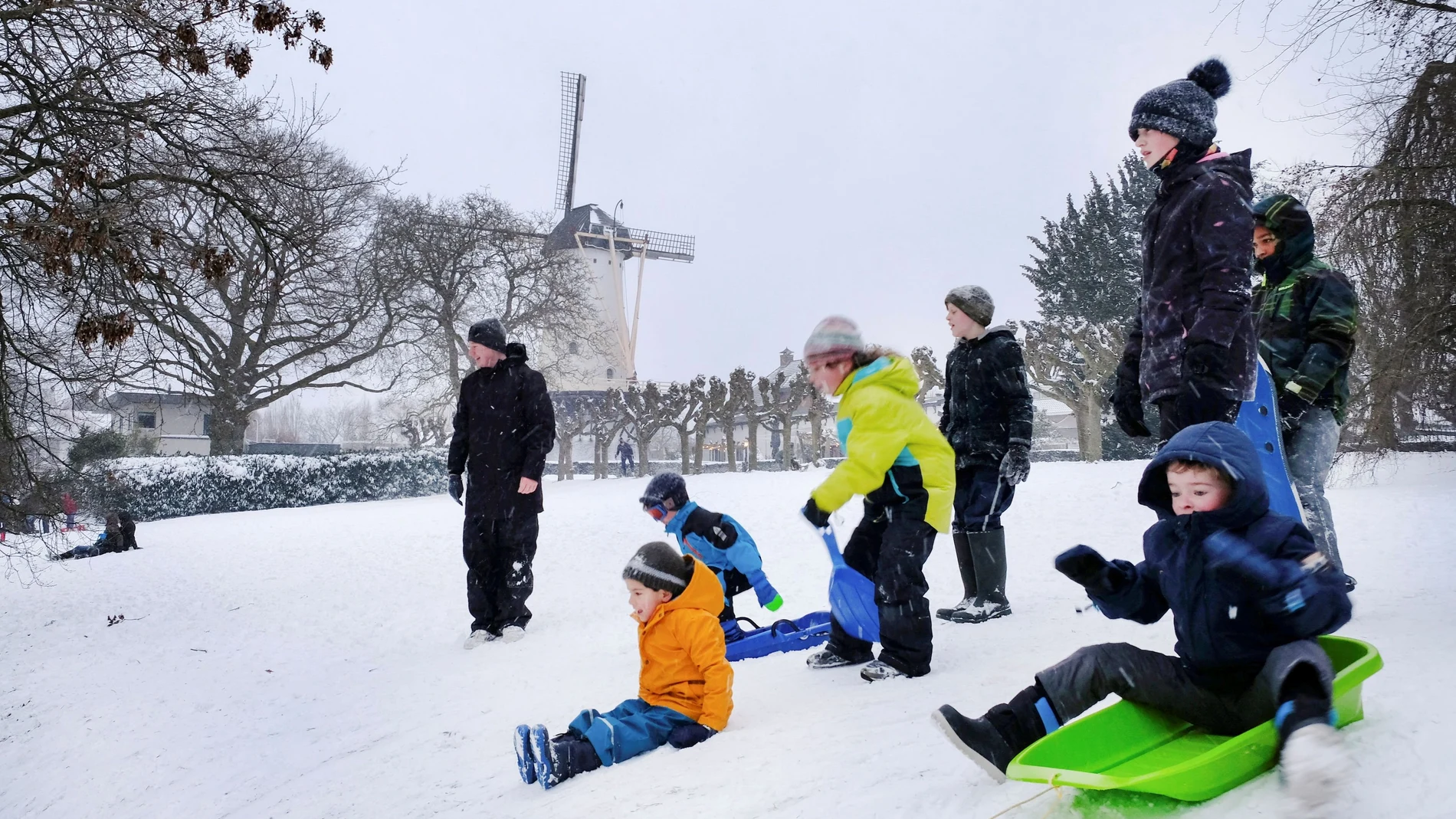 Unos niños se deslizan en trineo cerca de un molino de viento mientras nieva en Nijmegen, Países Bajos