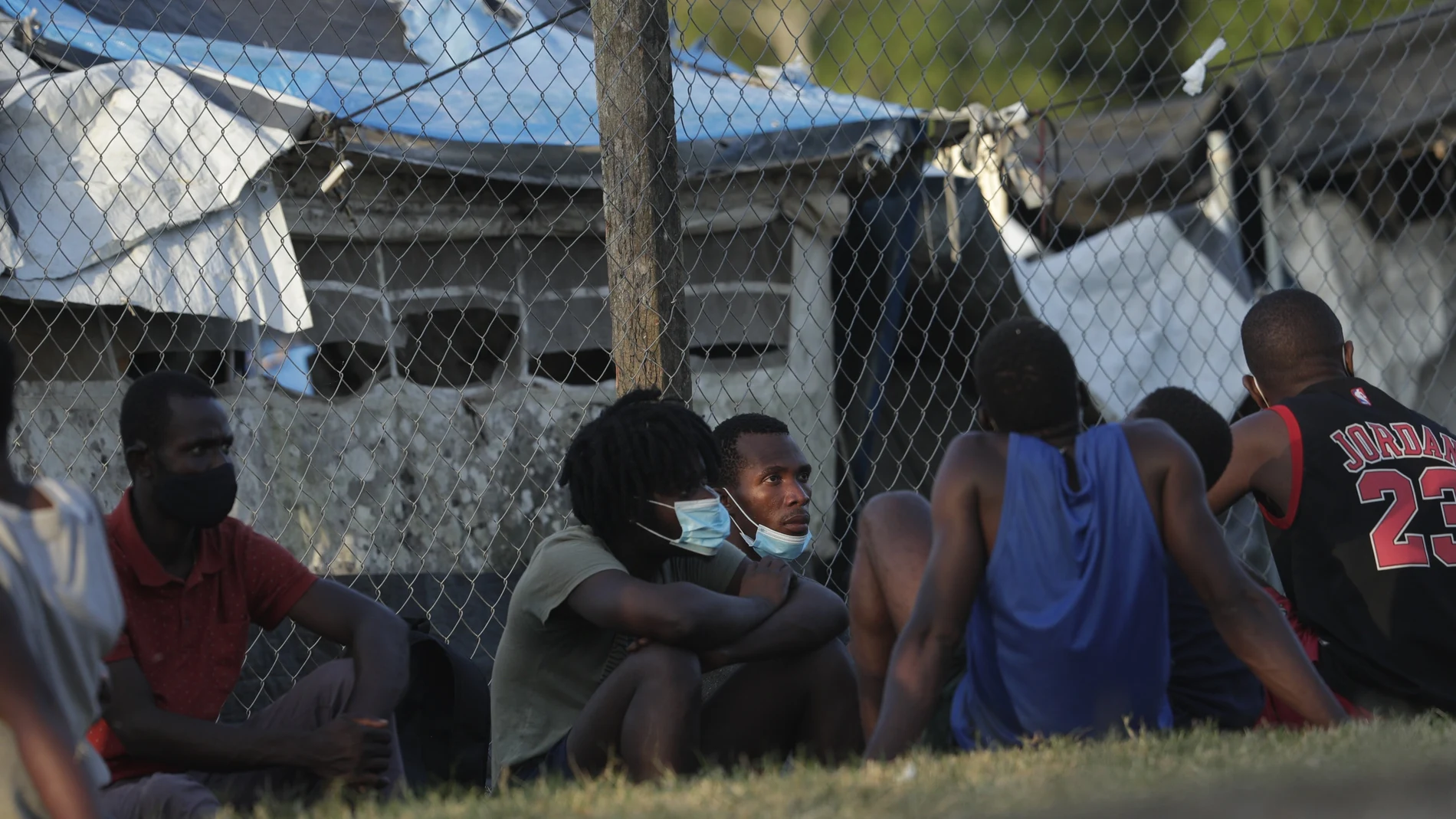 Haitian migrants sit on the grass at a migrant camp amid the new coronavirus pandemic in San Vicente, Darien province, Panama, Tuesday, Feb. 9, 2021. Panama is allowing hundreds of migrants stranded because of the pandemic, to move to the border with Costa Rica, after just reopening its land borders. (AP Photo/Arnulfo Franco)