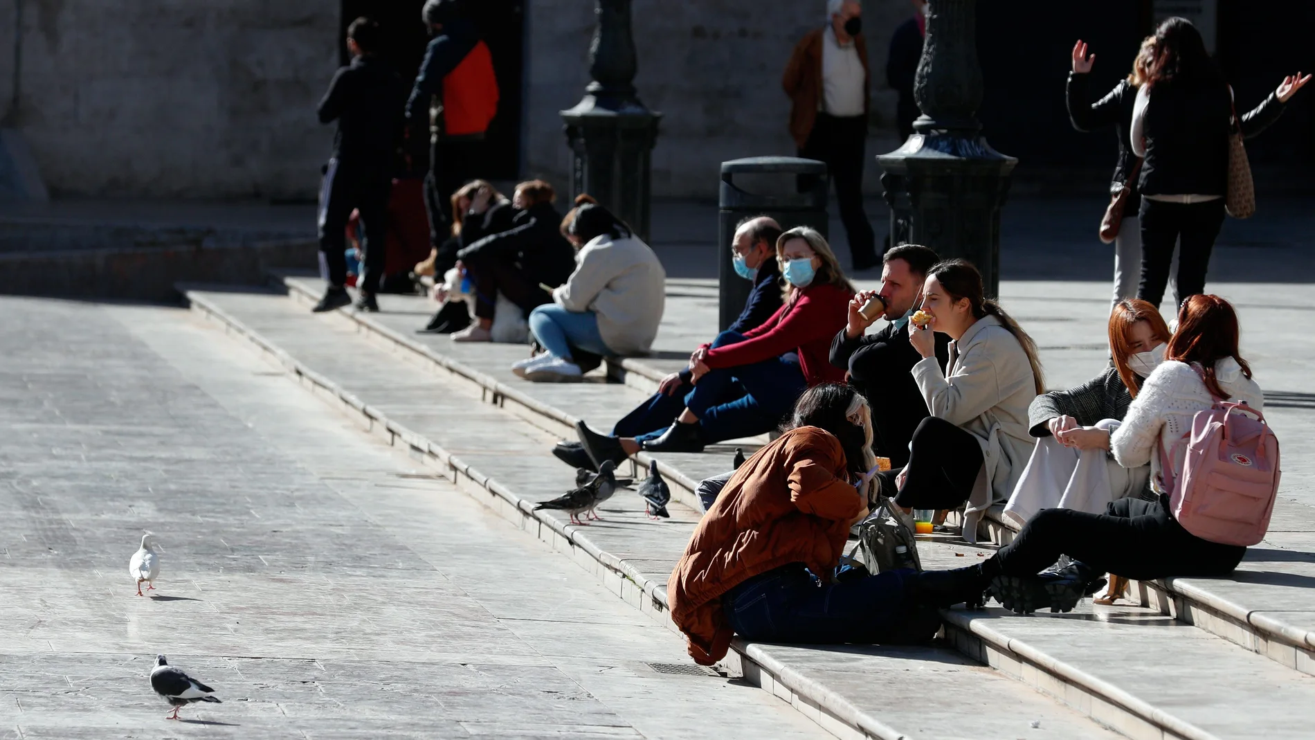 Un grupo de jóvenes almuerzan al sol en la Plaza de la Virgen de Valencia