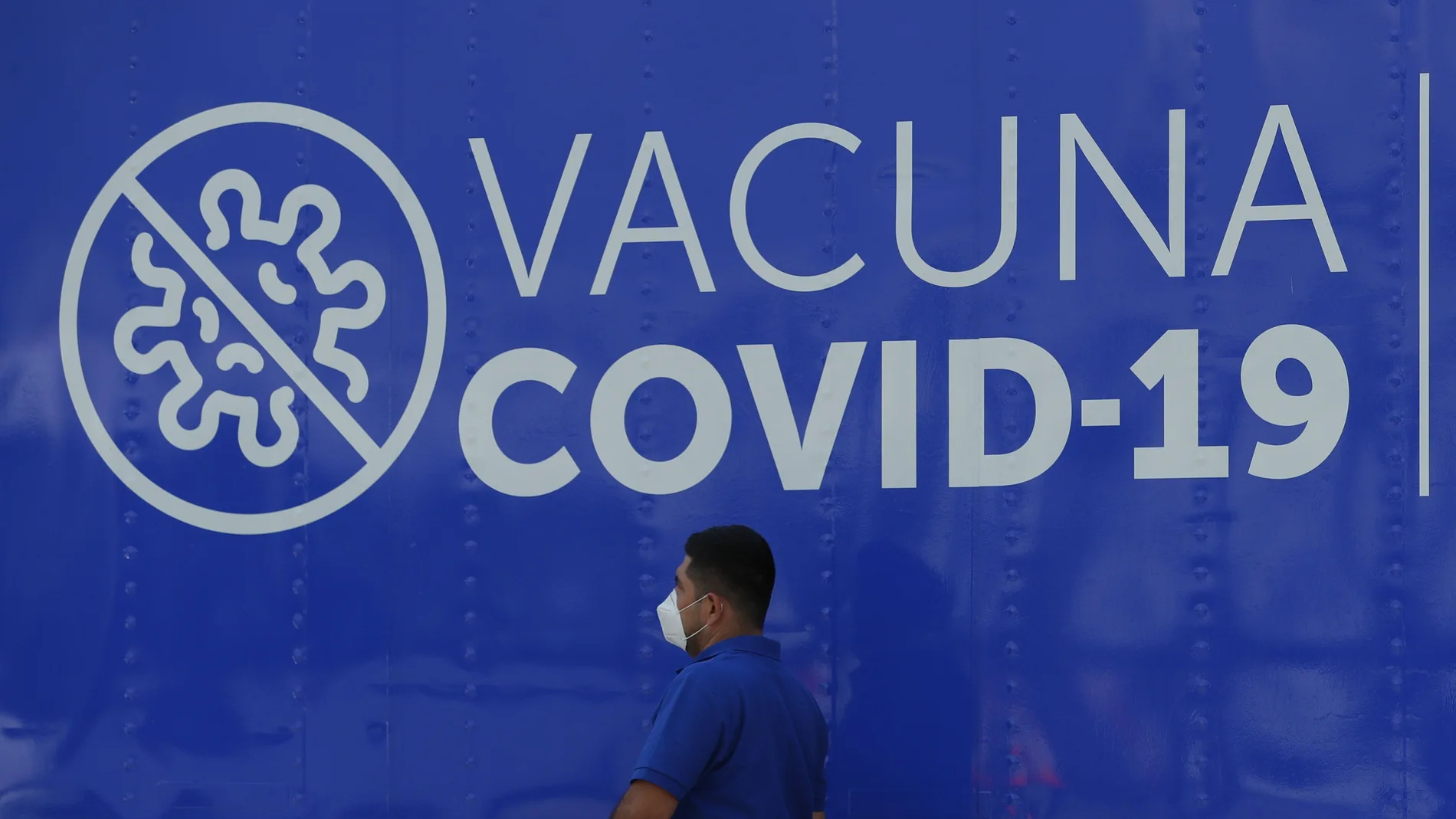 Un hombre camina frente a un anuncio de vacuna contra la covid-19 en San Salvador.
