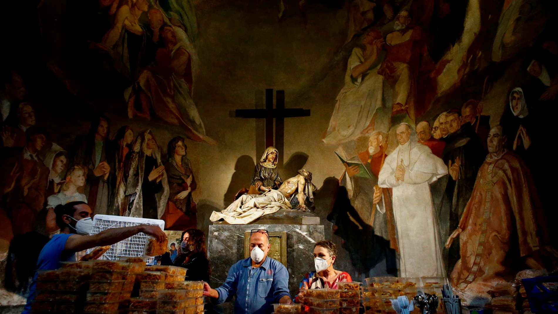 Varios voluntarios en la Capilla de la Pasión de la iglesia de Santa Anna de Barcelona preparan la comida que repartirán al día siguiente a más de 200 personas este lunes, sexagésimo quinto día del estado de alarma por la pandemia de coronavirus