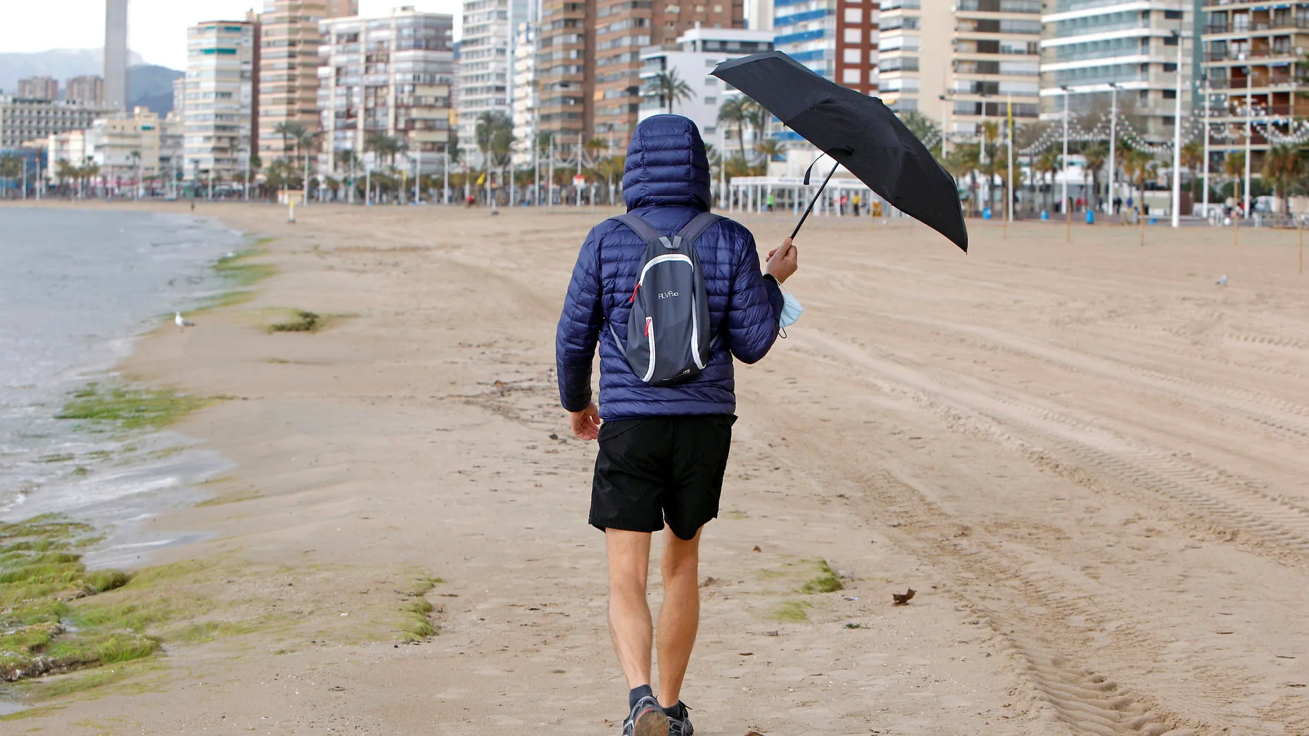 Una persona se protege de la lluvia con un paraguas mientras pasea por la playa de Levante de Benidor