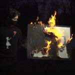 Un grupo de hombres ataviados con máscaras queman en directo la obra "Morons (White)" de Banksy