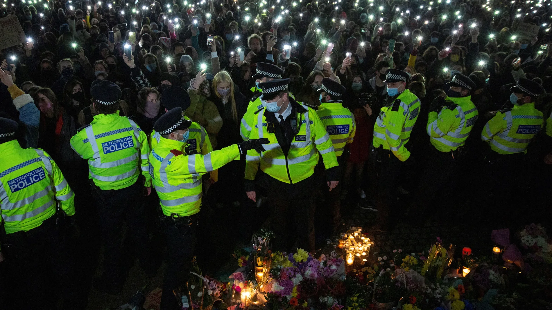 Los asistentes a una vigilia en memoria de Sarah Everard encienden las linternas de sus teléfonos móviles tras un cordón formado por agentes de la Policía Metropolitana de Londres (MET) , la noche del sábado en Clapham Common, Londres.