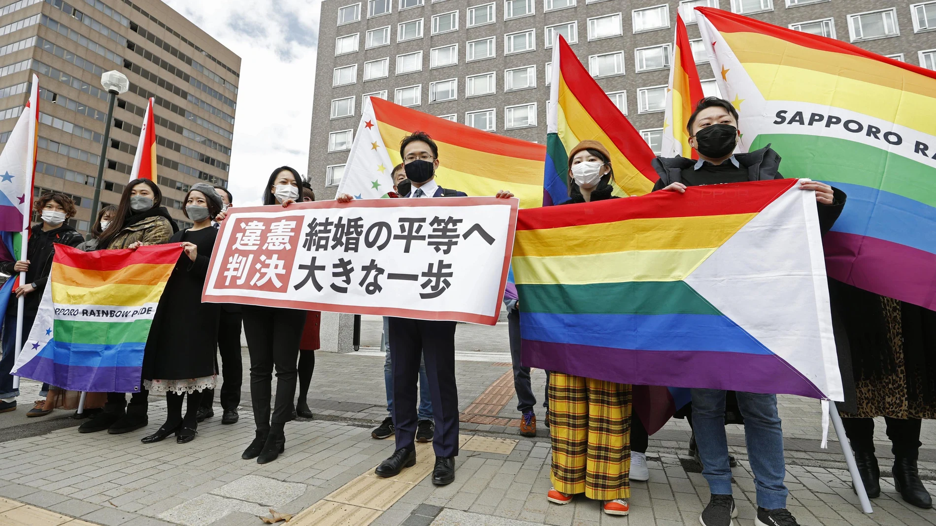 Los abogados y partidarios de los demandantes sostienen banderas de arcoíris y una pancarta que dice: "Sentencia inconstitucional"