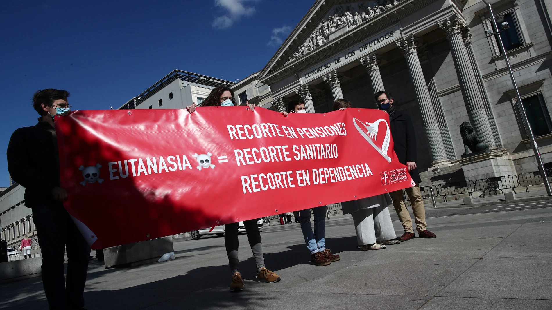 Varias personas sostienen una pancarta donde se puede leer "Recorte en pensiones, recorte sanitario, recorte en dependencia" durante una manifestación de Abogados Cristianos a las puertas del Congreso de los Diputados el 18 de marzo