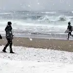 Dos chicas observan a un surfista momentos antes de meterse al agua, hoy en la playa de La Zurriola de San Sebastián, bajo una intensa nevada. EFE/Javier Etxezarreta