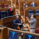 La ministra de Trabajo, Yolanda Díaz, aplaude al vicepresidente segundo del Gobierno, Pablo Iglesias (d), durante una sesión plenaria en el Congreso de los Diputados