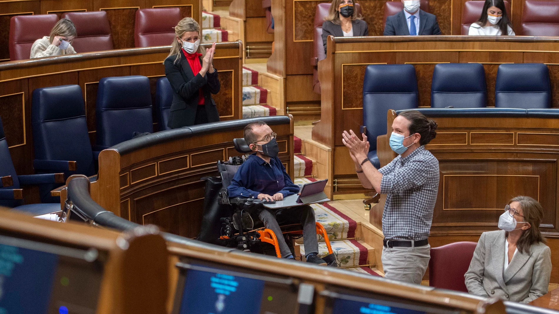 La ministra de Trabajo, Yolanda Díaz, aplaude al vicepresidente segundo del Gobierno, Pablo Iglesias (d), durante una sesión plenaria en el Congreso de los Diputados