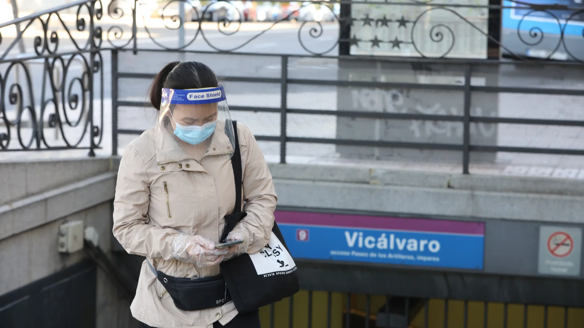Una mujer protegida con mascarilla y pantalla protectora espera en la entrada al metro de Vicálvaro