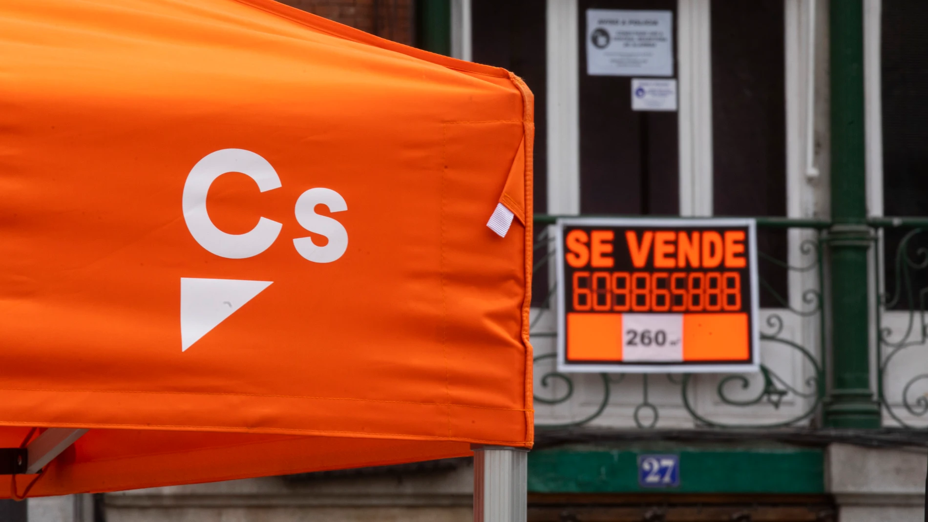 Imagen de una carpa electoral de Ciudadanos con un cartel de Se Vende al fondo