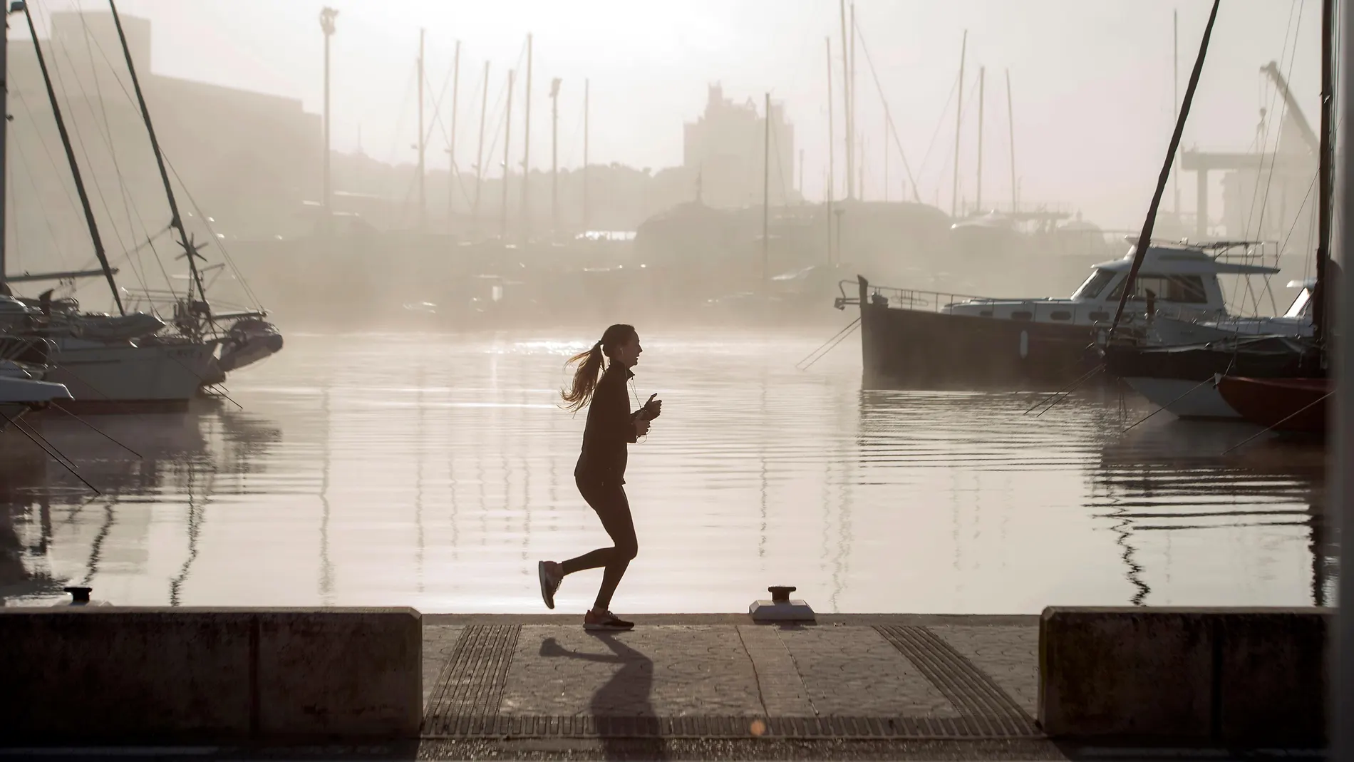 Una corredora practica deporte mientras la niebla cubre el Puerto de Mahón, Menorca