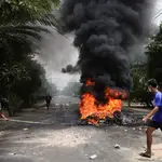 Varios manifestantes pasan junto a neumáticos en llamas después de que los activistas llevaran a cabo una &quot;huelga de basura&quot; contra la Junta Militar en Rangún