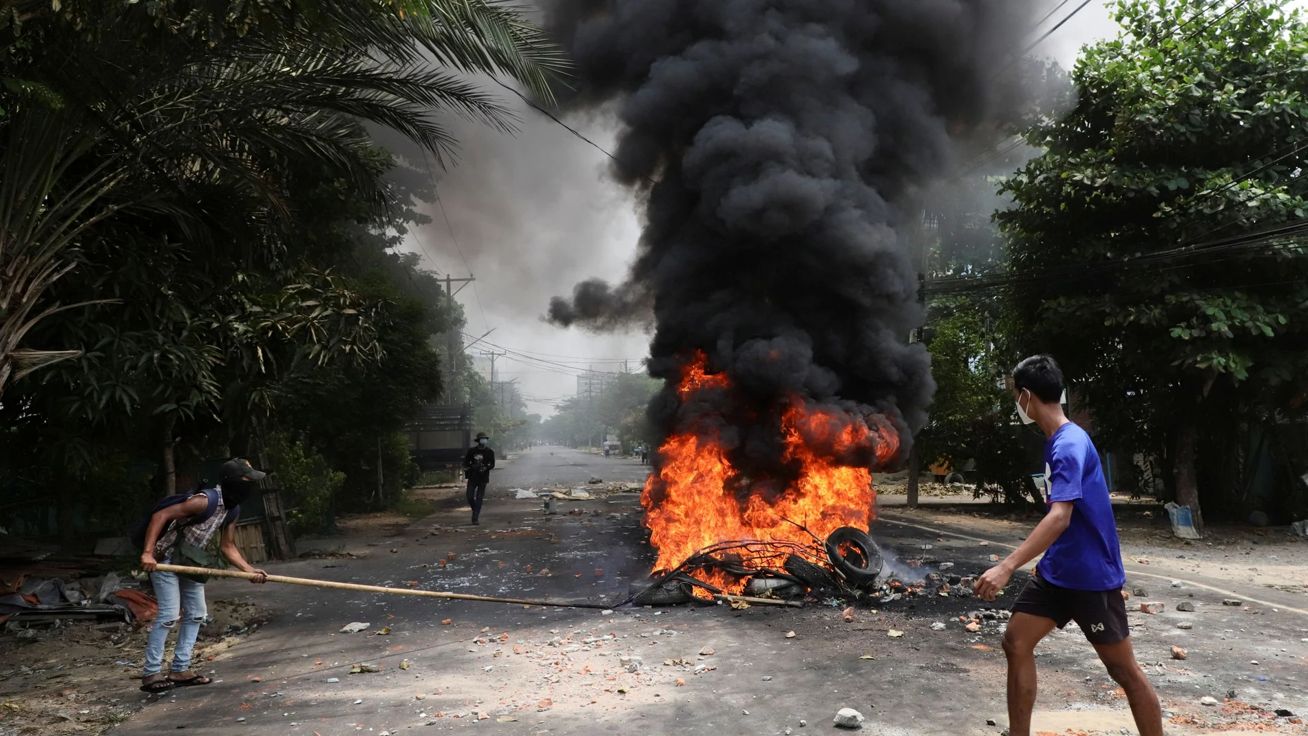 Varios manifestantes pasan junto a neumáticos en llamas después de que los activistas llevaran a cabo una "huelga de basura" contra la Junta Militar en Rangún