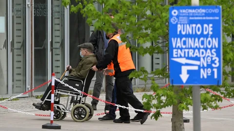Un operario ayuda a un hombre que va a ser vacunado con la dosis de Pfizer en el pabellón de Expocoruña