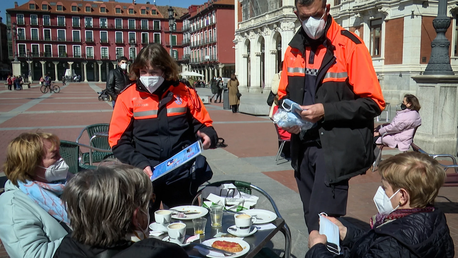 Voluntarios de Protección Civil informan sobre las medidas sanitarias a tres clientas de una terraza de Valladolid