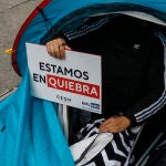 Un trabajador del ocio nocturno con un cartel en el que se lee: "Estamos en quiebra", participa en una concentración hoy en la plaza de Manises de Valencia