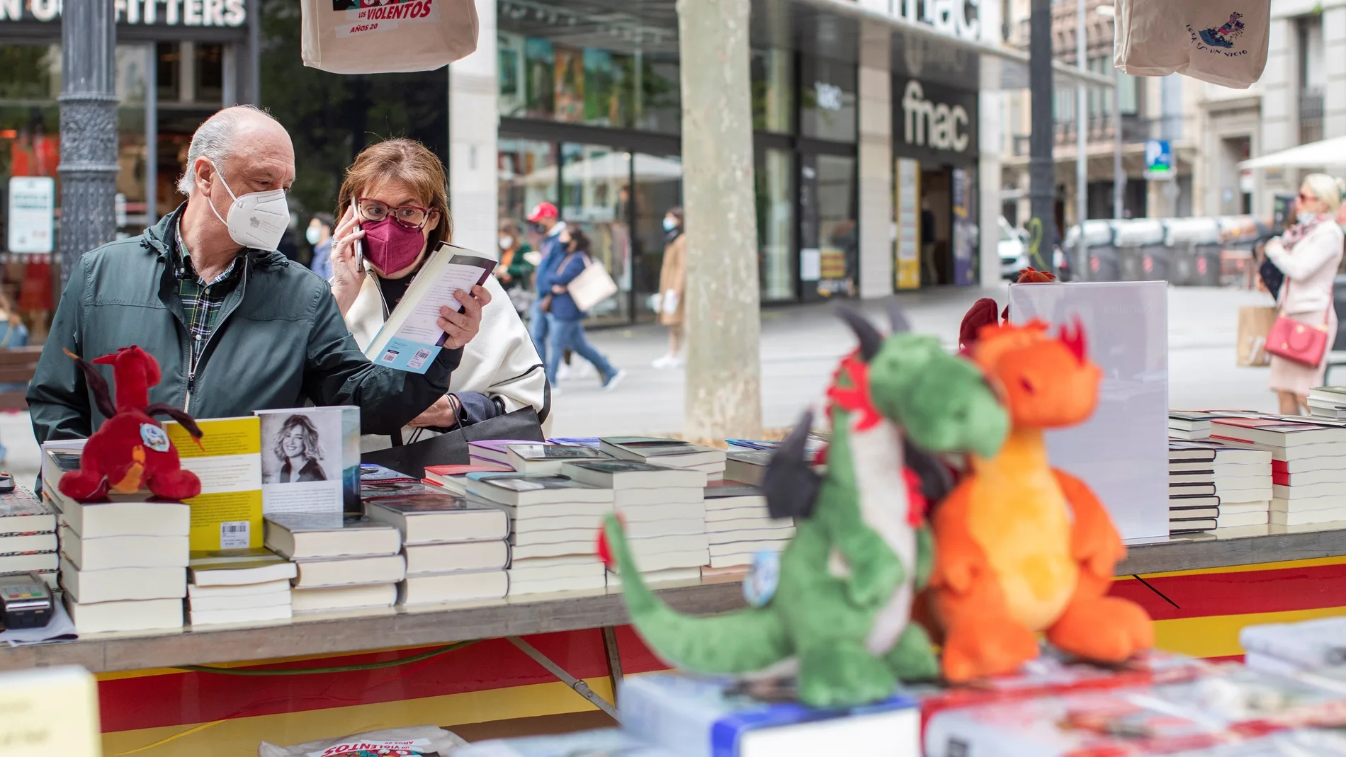 Unos clientes buscan libros en una conocida librería del centro de Barcelona, que ha colocado su puesto de venta en la calle para anticipar y evitar las habituales aglomeraciones en su establecimiento mañana Diada de Sant Jordi, día del libro y de la rosa.