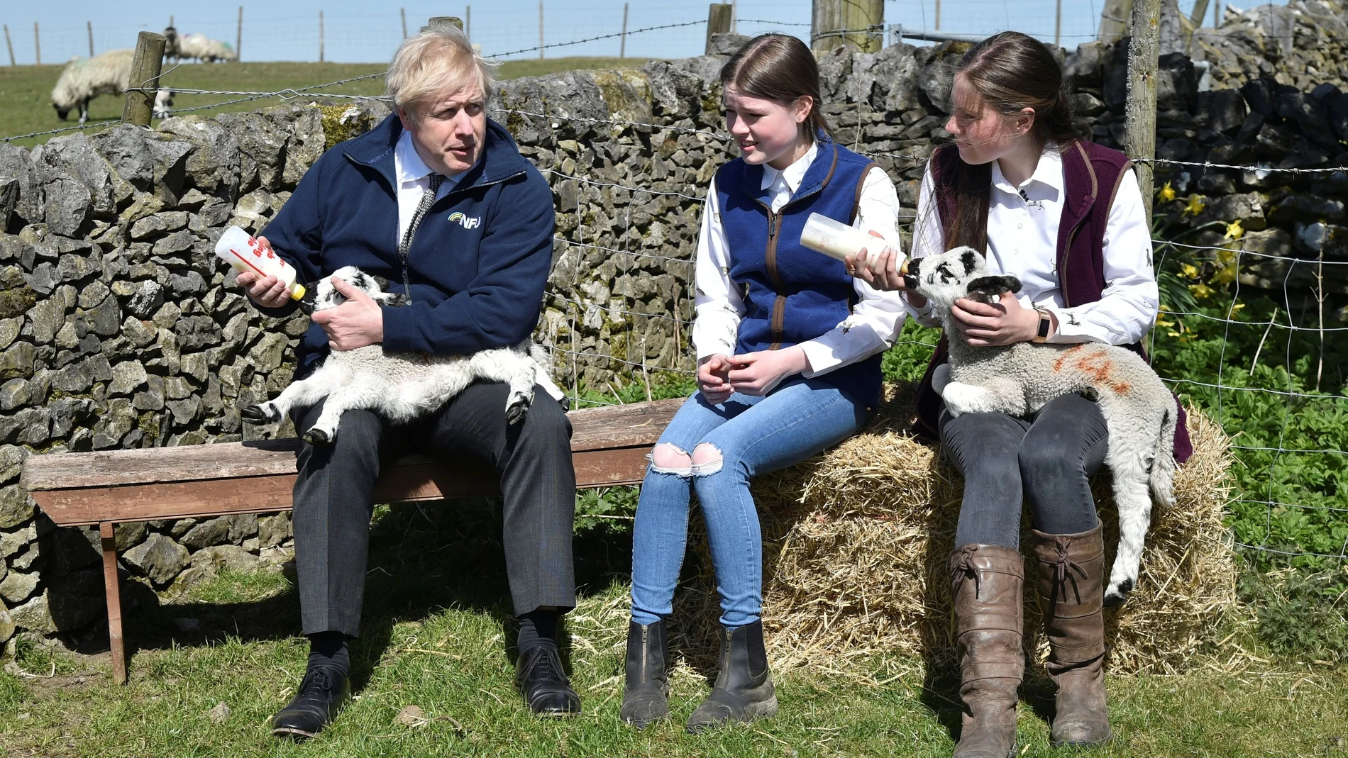 El primer ministro británico, Boris Johnson, da el biberón a un cordero recién nacido junto a dos estudiantes en una granja de Stoney Middleton