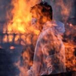 Un trabajador municipal con EPI tras las llamas de una de las hogueras prendidas en un crematorio para víctimas de la Covid-19 en Bombay