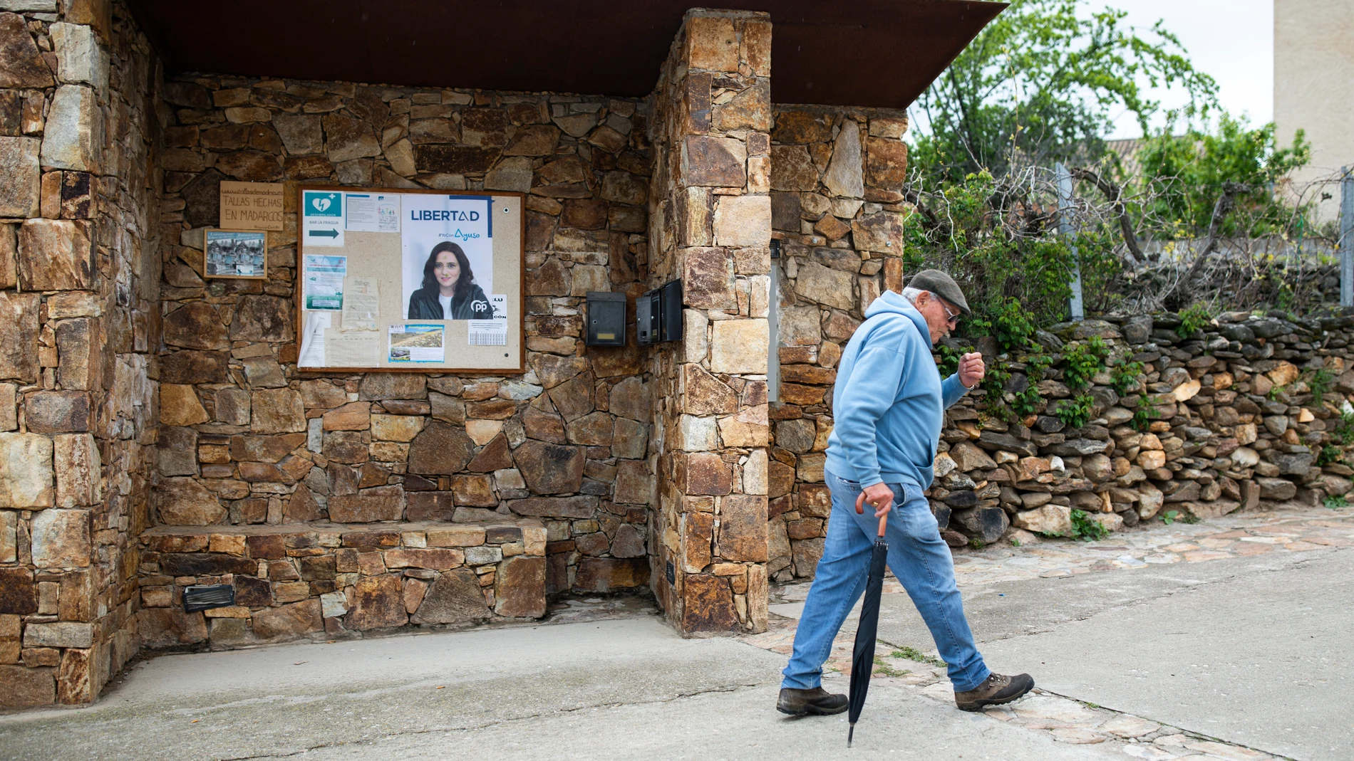 Un hombre pasa por delante de varios carteles electorales de Isabel Díaz Ayuso, en Madarcos