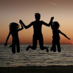 Una madre y sus hijas son felices y saltan en la puesta del sol con el mar de fondo