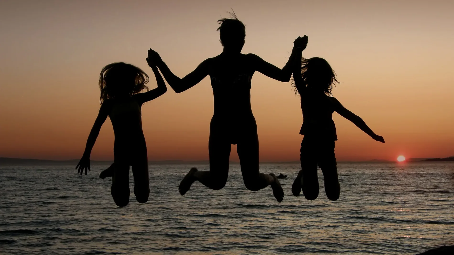 Una madre y sus hijas son felices y saltan en la puesta del sol con el mar de fondo