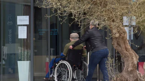 Una mujer pasea junto a un anciano en silla de ruedas