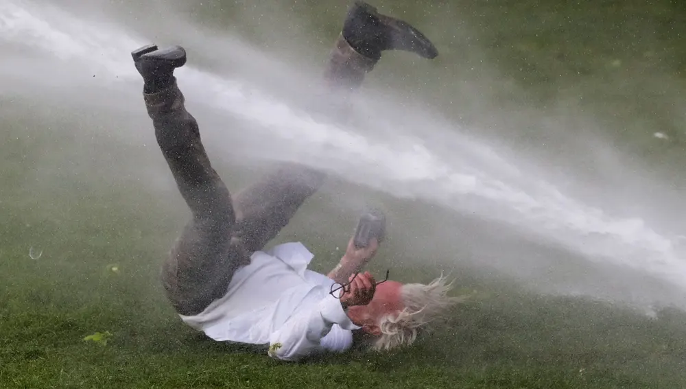 Un hombre es derribado con un cañón de agua en las protestas en Bruselas contra las restricciones por la covid