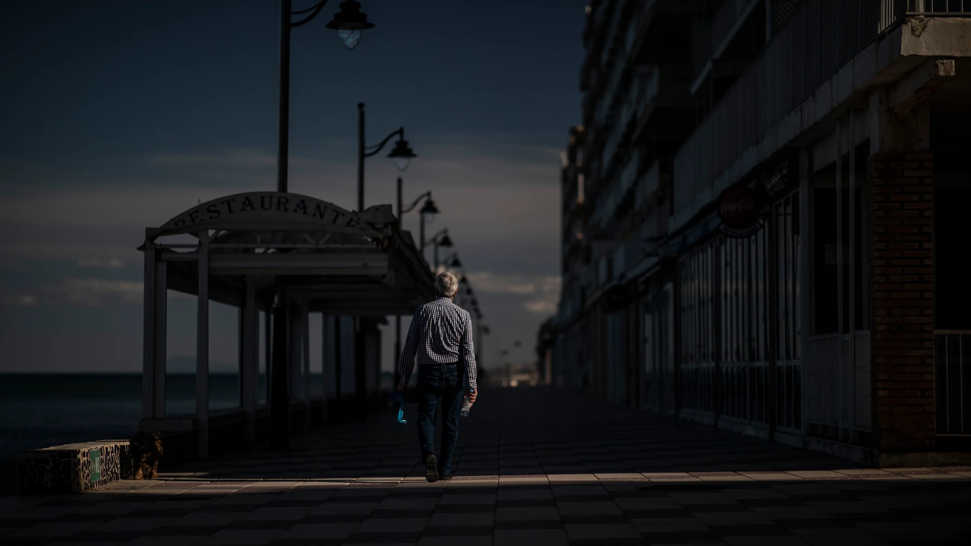 Un hombre pasea solitario por el paseo marítimo de Valencia sin llevar puesta la mascarilla