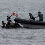 Miembros de la Guardia Civil lanzan un flotador a varios menores que esperan encima de unas rocas en la playa ceutí de El Tarajal