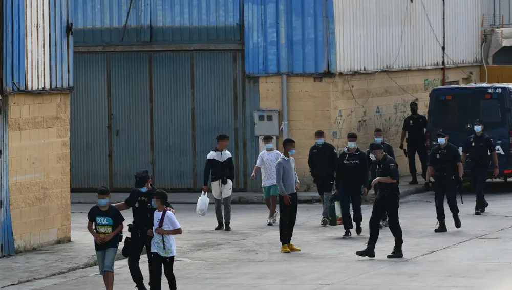 Agentes de la Policía Nacional acompañan a menores marroquíes a las naves acondicionadas anexas a la frontera del Tarajal en Ceuta