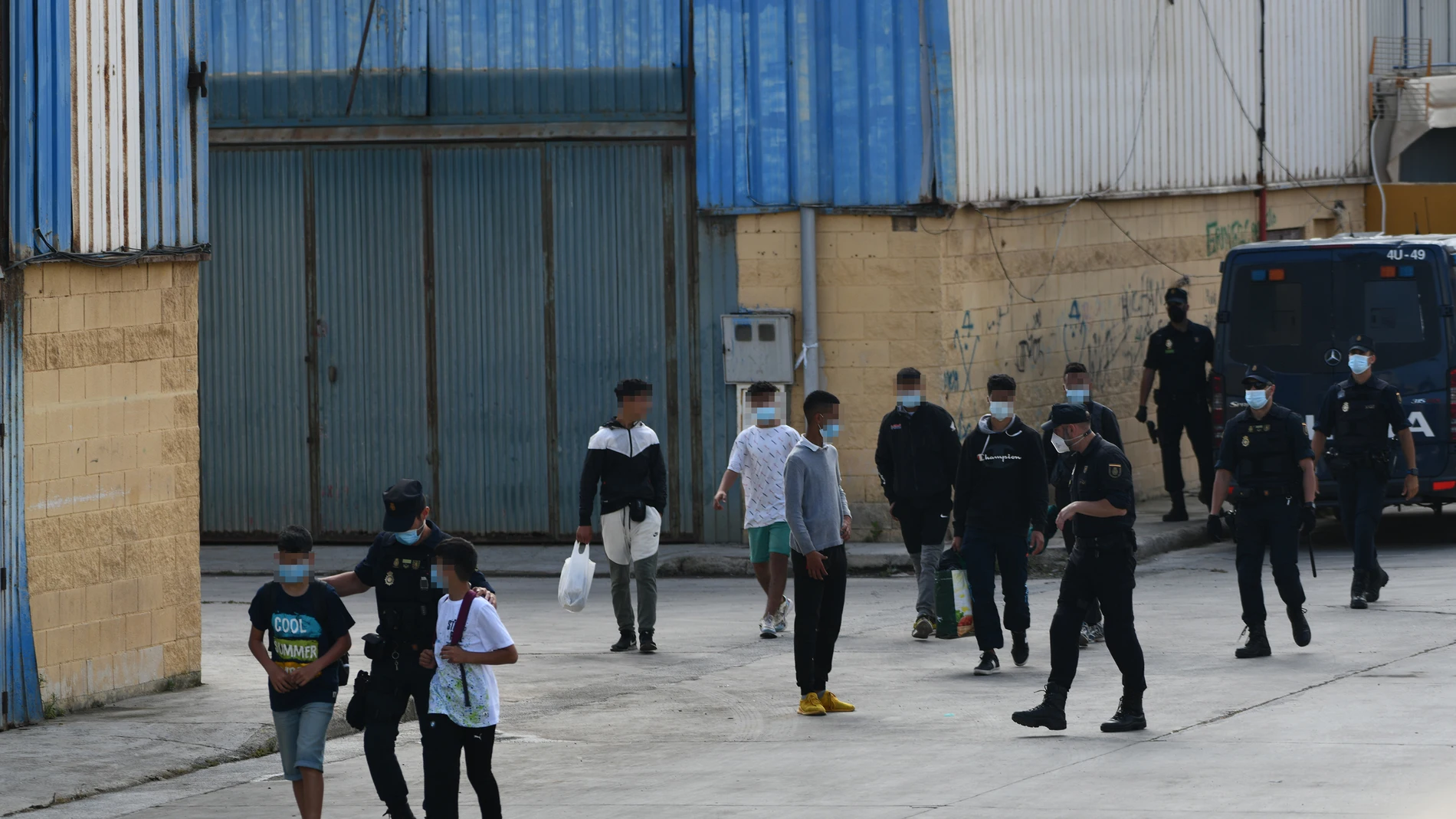Agentes de la Policía Nacional acompañan a menores marroquíes a las naves acondicionadas anexas a la frontera del Tarajal en Ceuta