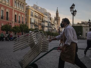 Un camarero recoge el mobiliario de la terraza de un bar en Sevilla