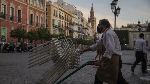 Un camarero recoge el mobiliario de la terraza de un bar en Sevilla