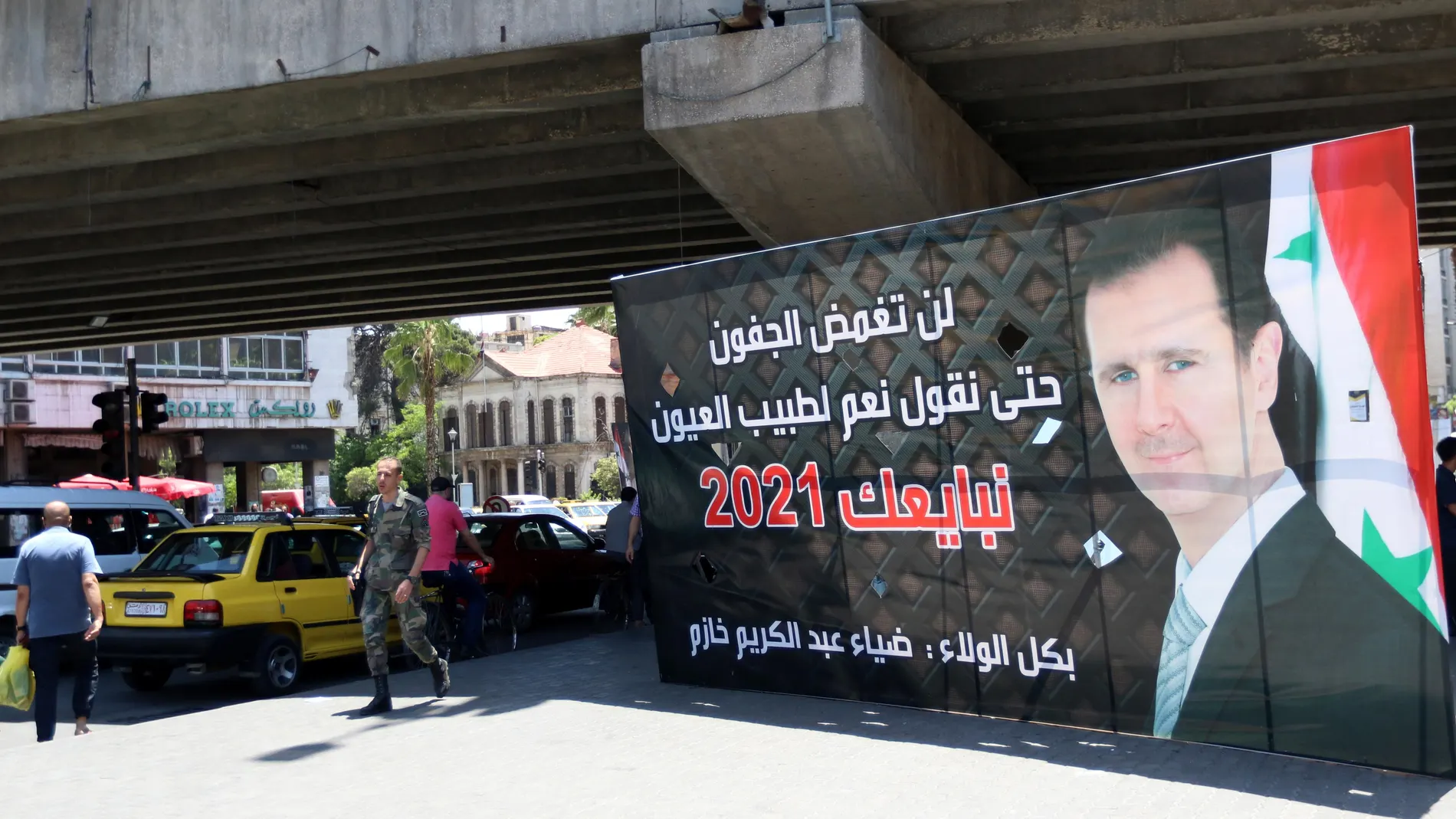 Varios peatones pasa junto a un cartel electoral que muestra al presidente sirio, Bachar Al Assad, en Damasco