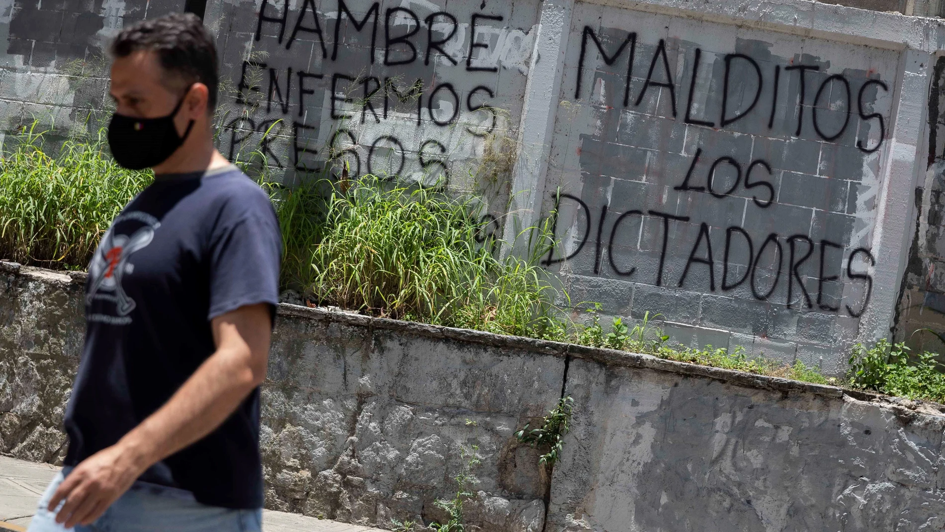 Un hombre camina frente a grafitis que dicen "Hambre, enfermos, presos. Malditos los dictadores", en Caracas