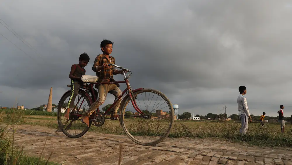 Dos niños indios montan en bicicleta por el campo.