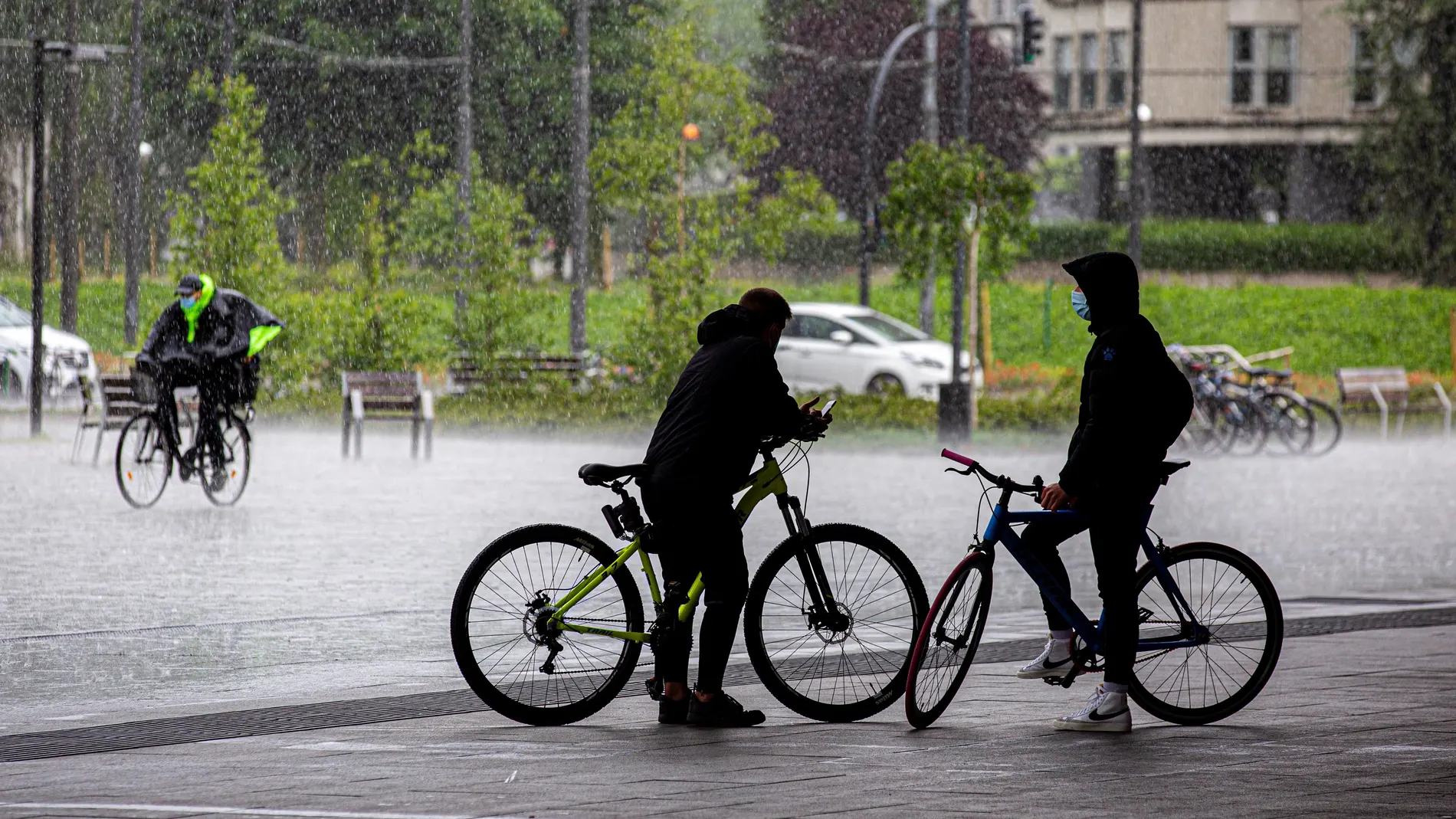 Dos ciclistas se resguardan de una tormenta en Vitoria, mientras un tercero pedalea bajo la lluvia
