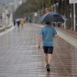 Un hombre camina bajo la lluvia por el Paseo Maritimo de Almería. EFE / Carlos Barba