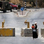 Una mujer palestina con un niño en brazos pasa junto a una patrulla militar israelí en Naplusa (Cisjordania)